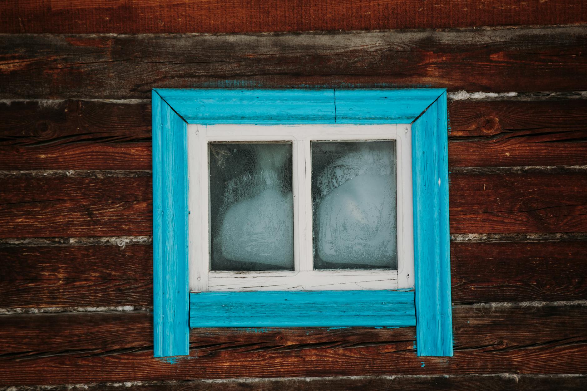 Stara drewniana ściana domu z niebieskim, obdrapanym oknem