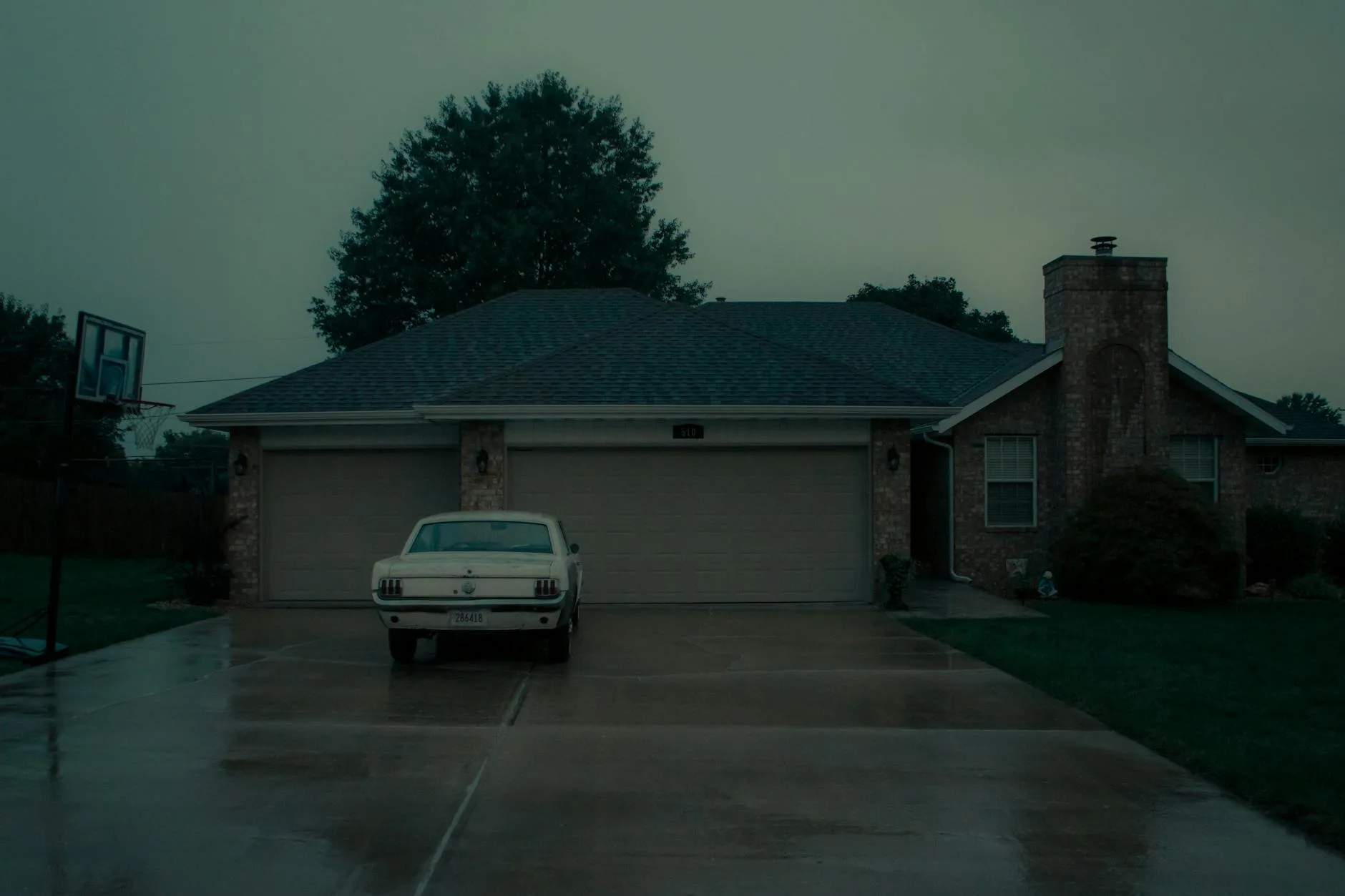 Stary samochód zaparkowany na mokrym podjeździe przy domu jednorodzinnym