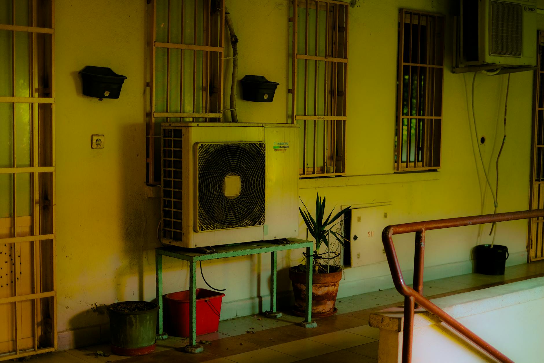 Zewnętrzna jednostka klimatyzacji na balkonie wśród doniczek z roślinami