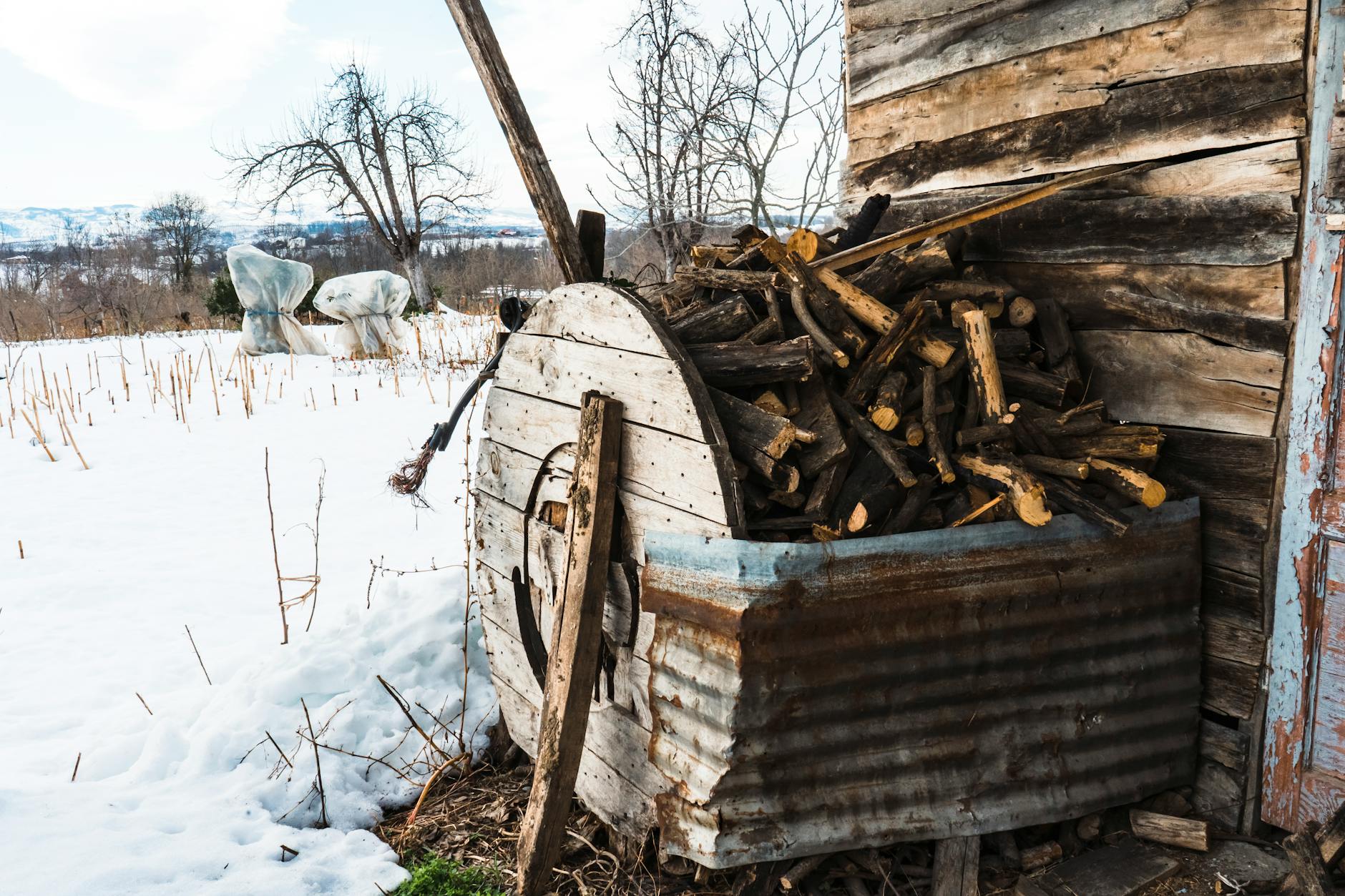 Drewniana wiata z polanami opałowymi obok starej stodoły w śniegu