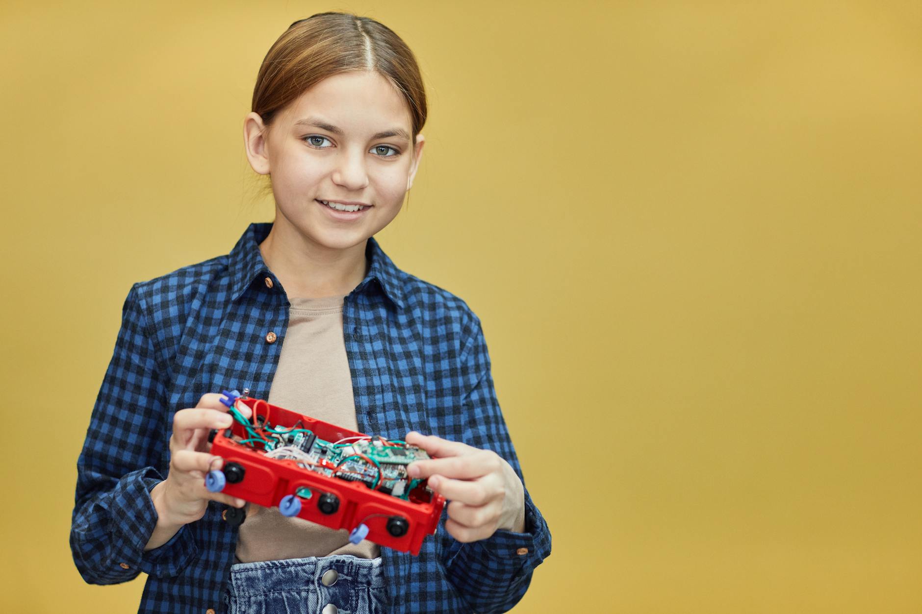 Uśmiechnięta dziewczynka trzyma zestaw do robotyki na żółtym tle