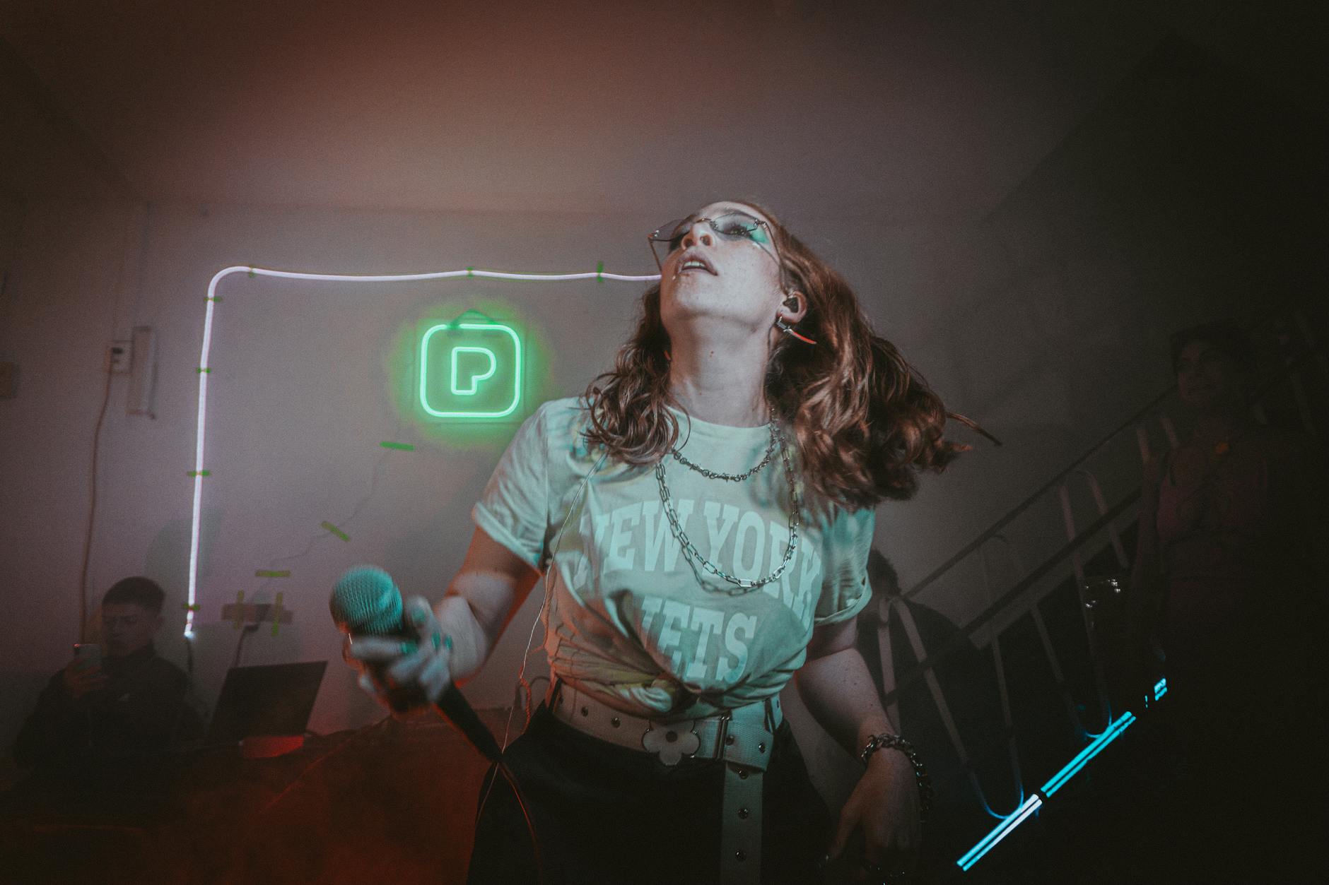 Wokalistka śpiewa energicznie na neonowej scenie podczas koncertu