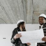 Dwóch architektów w kaskach analizuje plany na placu budowy domu