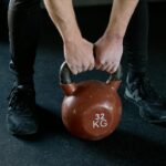 Osoba unosi kettlebell 32 kg na treningu siłowym w siłowni