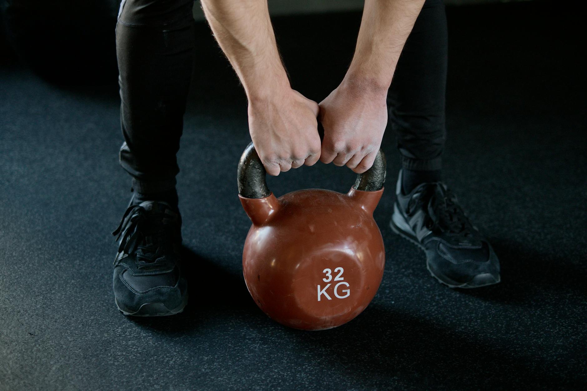 Osoba unosi kettlebell 32 kg na treningu siłowym w siłowni