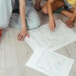 Para analizuje plany rozbudowy domu rozłożone na jasnej podłodze
