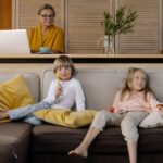 Babcia pracuje na laptopie w salonie, obok odpoczywają wnuki na kanapie