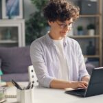Mama pracująca zdalnie przy laptopie, dziecko bawi się w tle
