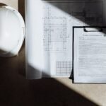 Dokumenty budowlane i kask ochronny w słońcu widziane z góry